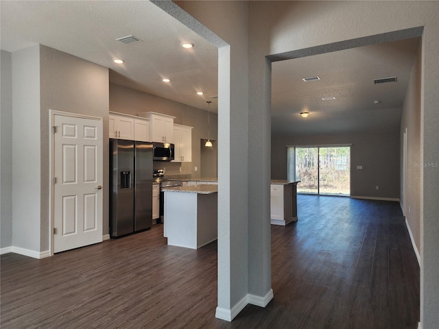 kitchen with appliances with stainless steel finishes, light stone counters, white cabinets, and dark hardwood / wood-style flooring