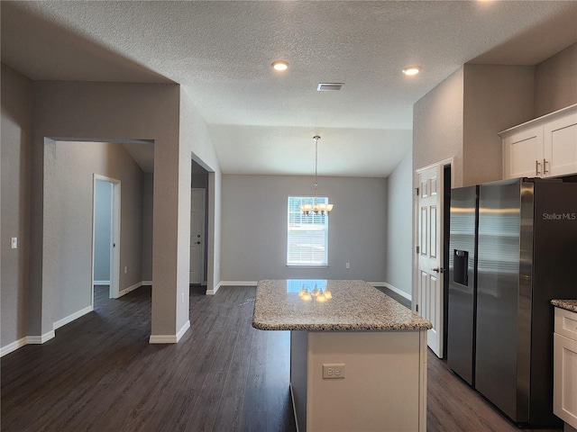 kitchen featuring stainless steel fridge, light stone countertops, white cabinets, a kitchen island, and decorative light fixtures