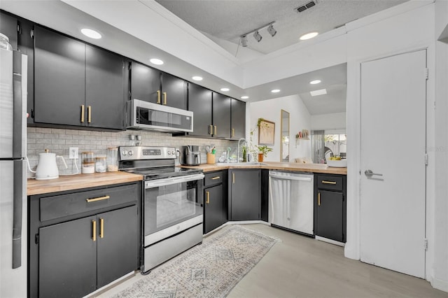 kitchen with rail lighting, butcher block counters, sink, stainless steel appliances, and a textured ceiling