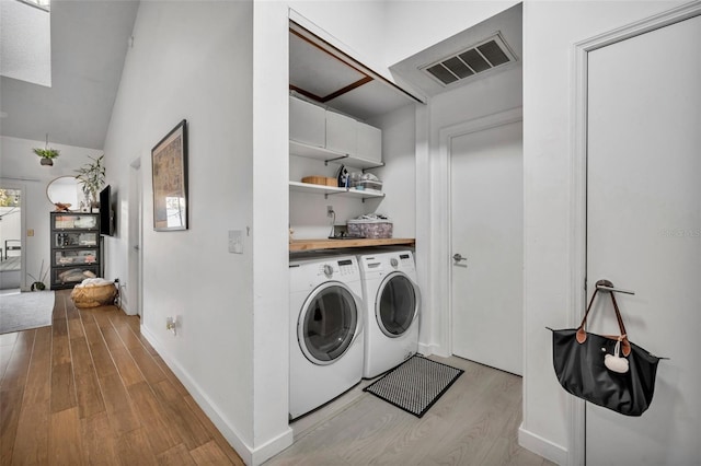 clothes washing area with washing machine and dryer and light wood-type flooring