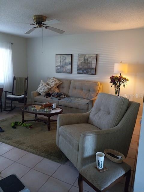 living room with ceiling fan, a textured ceiling, and light tile patterned floors