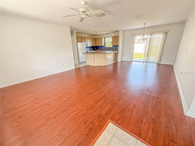 unfurnished living room featuring a textured ceiling, ceiling fan with notable chandelier, baseboards, ornamental molding, and light wood-type flooring