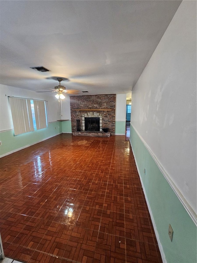 unfurnished living room featuring dark parquet flooring, a fireplace, and ceiling fan