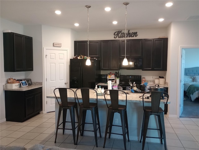 kitchen with pendant lighting, a center island with sink, light tile patterned floors, and black appliances