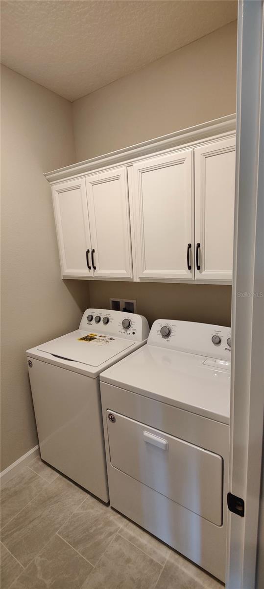 clothes washing area featuring cabinets, washing machine and dryer, and a textured ceiling