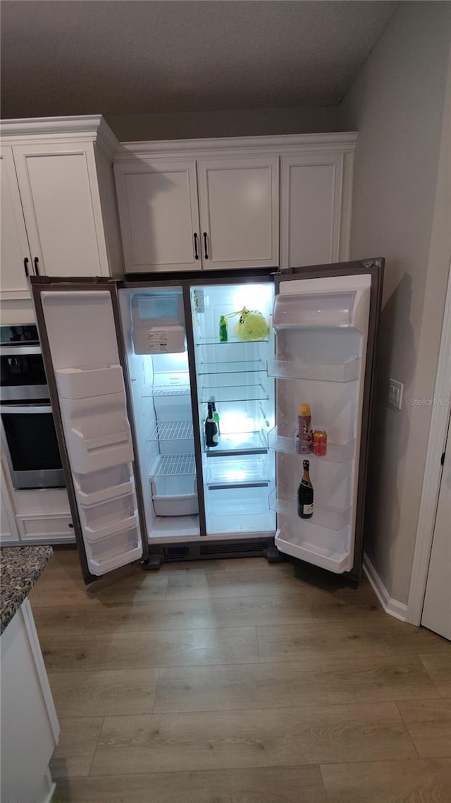 kitchen with refrigerator, light hardwood / wood-style flooring, dark stone countertops, stainless steel double oven, and white cabinets