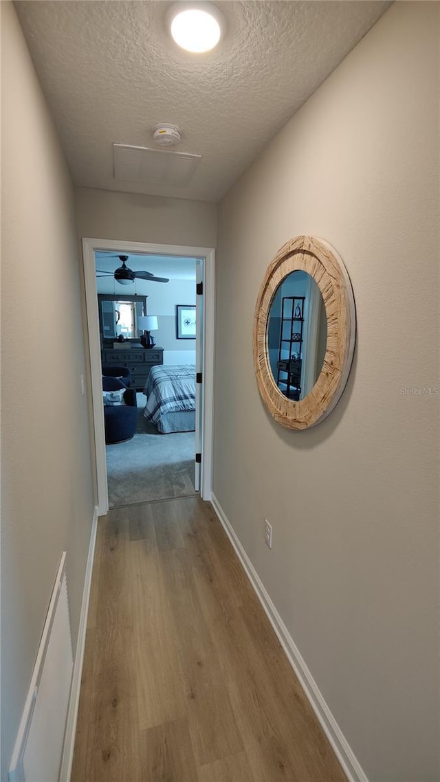 hall with a textured ceiling and light wood-type flooring