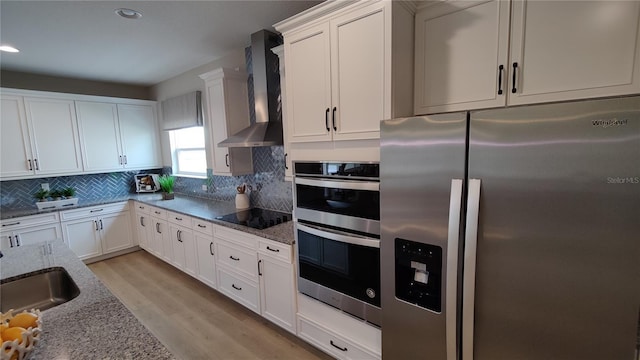 kitchen with wall chimney exhaust hood, stainless steel appliances, light stone countertops, and white cabinets