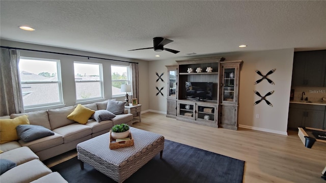 living room featuring ceiling fan, sink, a textured ceiling, and light wood-type flooring