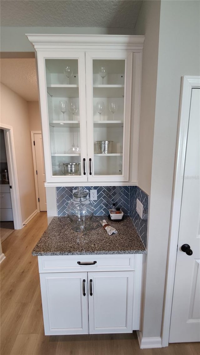 bar featuring white cabinetry, decorative backsplash, and dark stone countertops