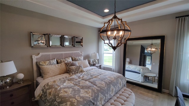 bedroom featuring a raised ceiling, wood-type flooring, and a notable chandelier