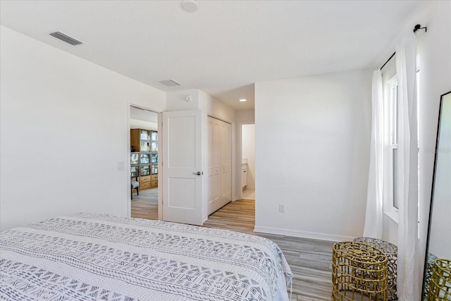 bedroom featuring hardwood / wood-style flooring, ensuite bath, multiple windows, and a closet