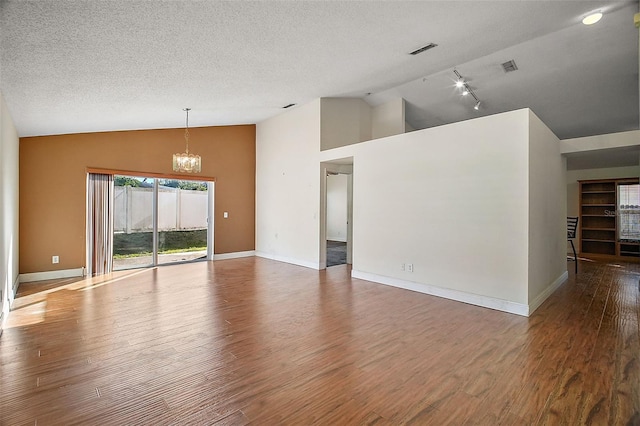 unfurnished living room with rail lighting, vaulted ceiling, a textured ceiling, dark hardwood / wood-style flooring, and a notable chandelier