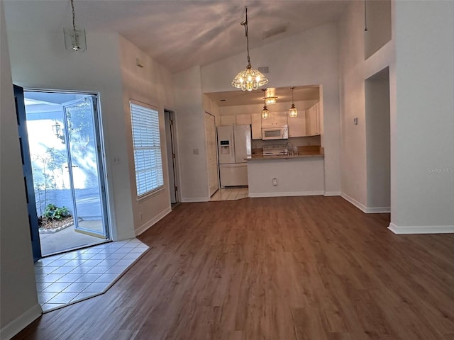 unfurnished living room featuring high vaulted ceiling, sink, a chandelier, and light hardwood / wood-style floors