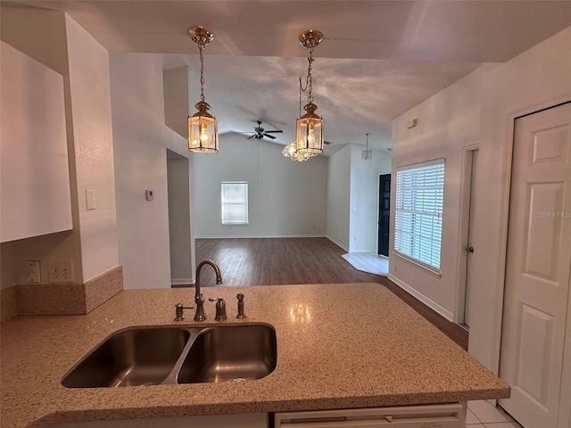 kitchen featuring dishwashing machine, sink, hanging light fixtures, light stone counters, and kitchen peninsula