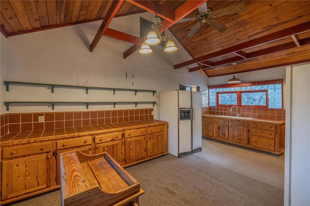 kitchen featuring pendant lighting, tile countertops, white refrigerator with ice dispenser, and vaulted ceiling with beams