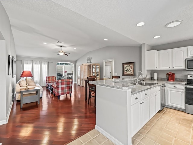 kitchen with vaulted ceiling, appliances with stainless steel finishes, white cabinetry, sink, and kitchen peninsula