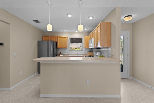 kitchen with range, light brown cabinets, stainless steel fridge, pendant lighting, and decorative backsplash