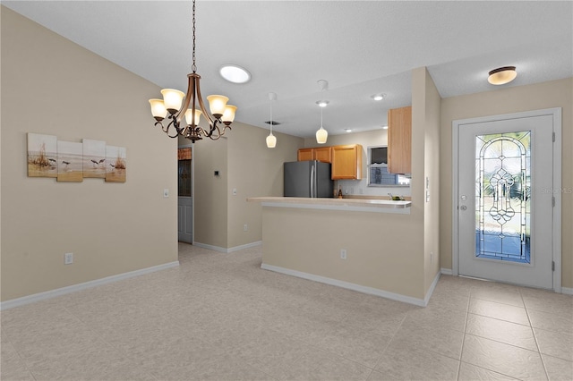 kitchen featuring light brown cabinetry, stainless steel refrigerator, hanging light fixtures, kitchen peninsula, and an inviting chandelier