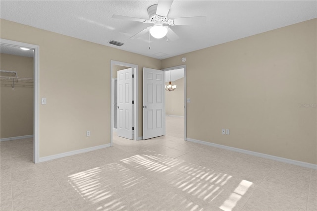 unfurnished bedroom with ceiling fan with notable chandelier, a walk in closet, light tile patterned floors, a textured ceiling, and a closet