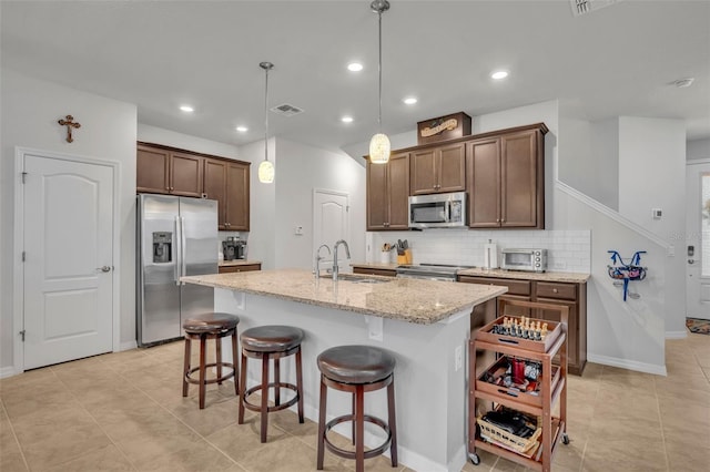 kitchen with visible vents, a center island with sink, a sink, stainless steel appliances, and decorative backsplash