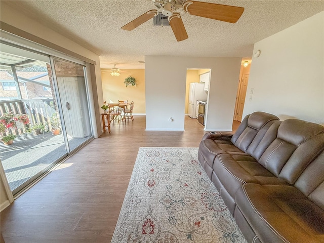 living room with ceiling fan, a textured ceiling, and light wood-type flooring