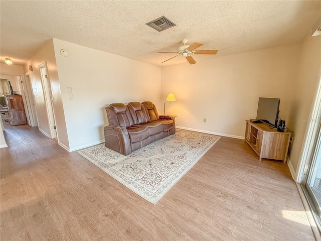 living room featuring ceiling fan, a textured ceiling, and light wood-type flooring