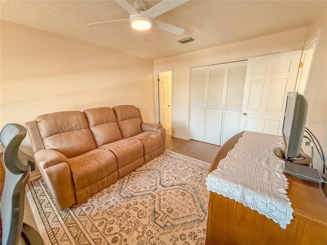 living room featuring ceiling fan, wood-type flooring, and a textured ceiling