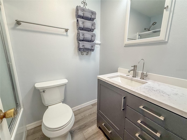 full bathroom with hardwood / wood-style flooring, bath / shower combo with glass door, vanity, and toilet