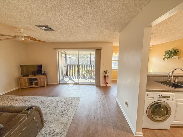 living room with washer / clothes dryer, hardwood / wood-style flooring, sink, and a textured ceiling