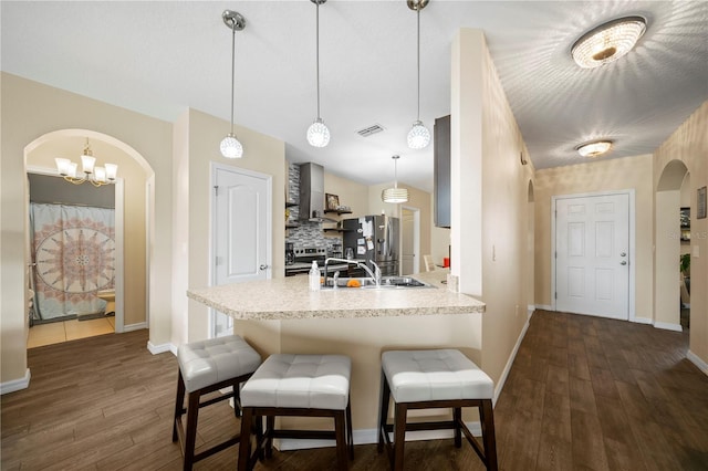 kitchen featuring wall chimney exhaust hood, dark hardwood / wood-style floors, kitchen peninsula, pendant lighting, and stainless steel appliances