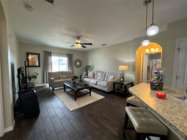 living area featuring baseboards, dark wood finished floors, ceiling fan with notable chandelier, arched walkways, and a textured ceiling