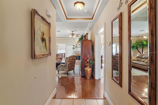 corridor with a raised ceiling, crown molding, and light tile patterned floors