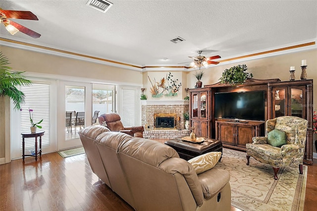 living room featuring wood-type flooring, a textured ceiling, a fireplace, and ceiling fan