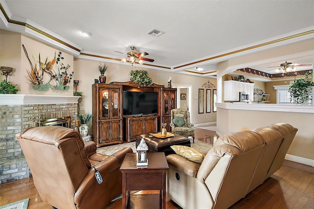 living room featuring hardwood / wood-style flooring, ceiling fan, a fireplace, and crown molding