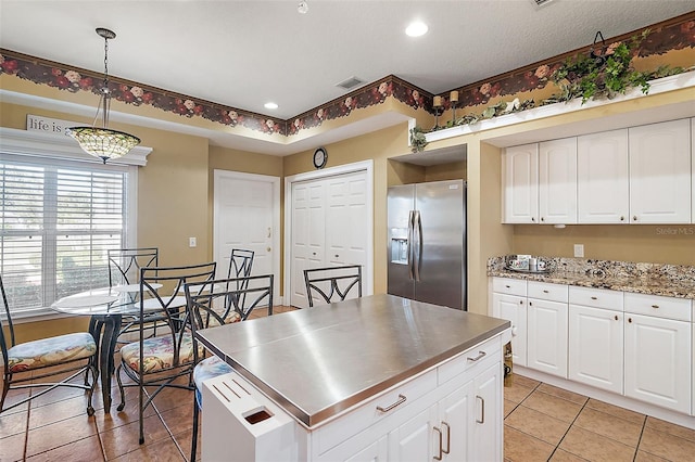 kitchen with light tile patterned floors, stainless steel fridge, white cabinets, a kitchen island, and decorative light fixtures