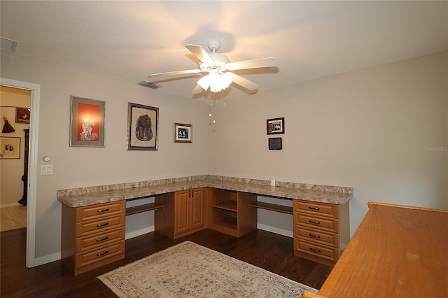 unfurnished office featuring ceiling fan, built in desk, and dark hardwood / wood-style flooring