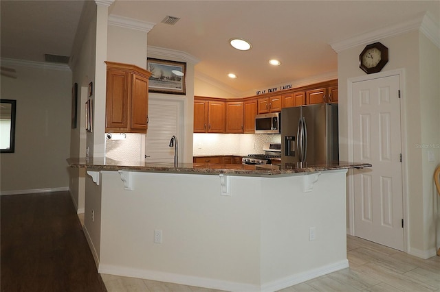 kitchen featuring stainless steel appliances, dark stone countertops, a kitchen bar, and kitchen peninsula