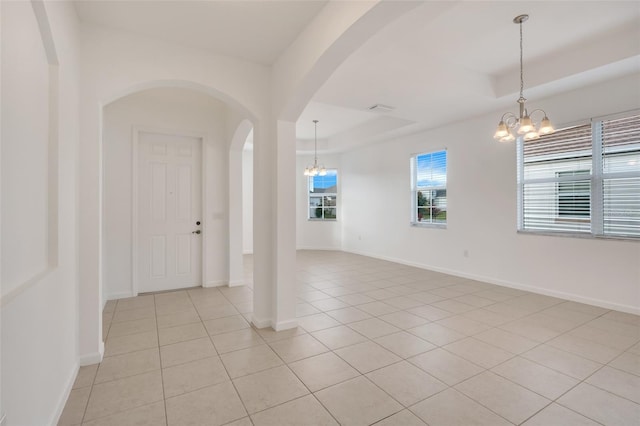 empty room featuring a raised ceiling, a chandelier, and light tile patterned flooring