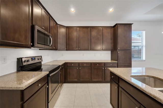 kitchen with stainless steel appliances, light tile patterned floors, dark brown cabinetry, and light stone counters