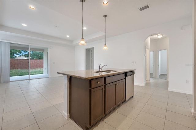 kitchen featuring dishwasher, a kitchen island with sink, hanging light fixtures, dark brown cabinets, and light stone counters