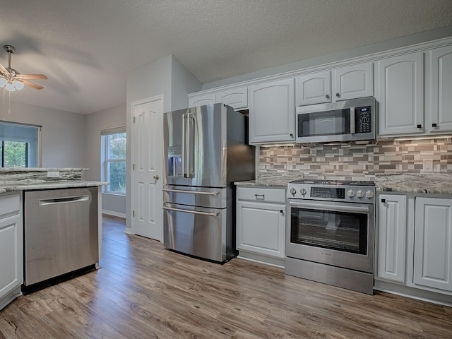 kitchen with stainless steel appliances, white cabinetry, light stone counters, and light hardwood / wood-style flooring