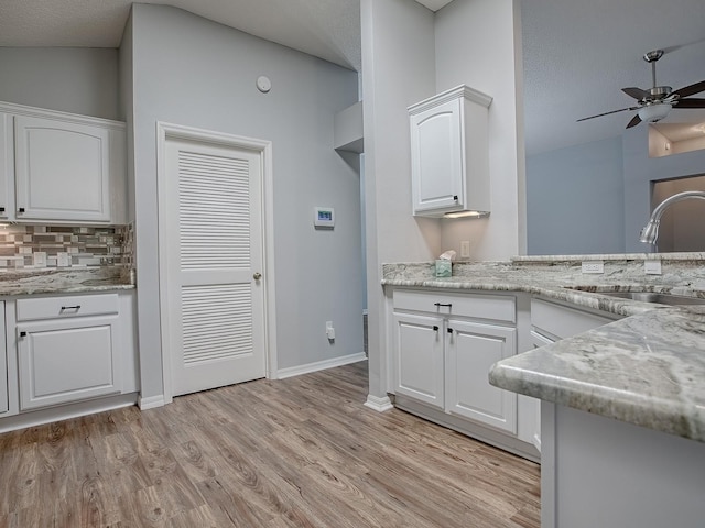 kitchen with sink, light stone counters, white cabinets, and light wood-type flooring