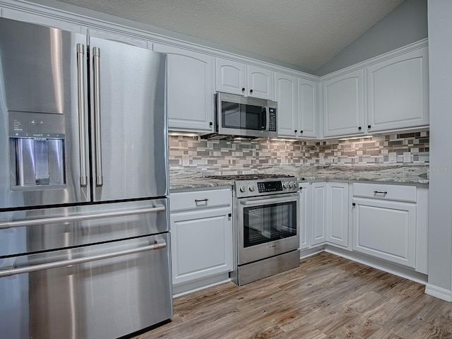 kitchen featuring light hardwood / wood-style flooring, stainless steel appliances, light stone countertops, white cabinets, and vaulted ceiling