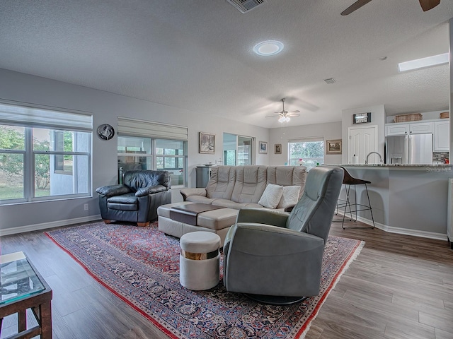 living room with a textured ceiling, ceiling fan, and light hardwood / wood-style flooring