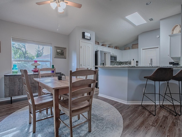 dining room featuring sink, a textured ceiling, dark hardwood / wood-style flooring, ceiling fan, and vaulted ceiling with skylight