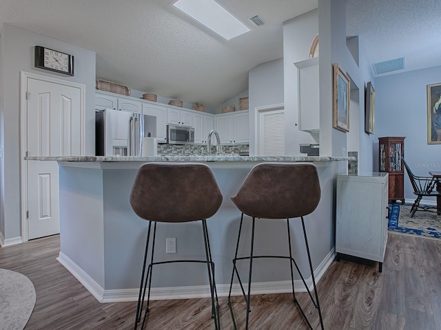 kitchen with lofted ceiling, sink, appliances with stainless steel finishes, hardwood / wood-style flooring, and white cabinets