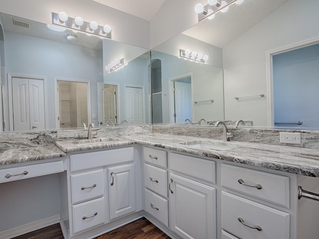 bathroom with vanity, vaulted ceiling, hardwood / wood-style floors, and a textured ceiling