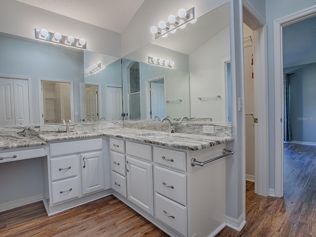 bathroom with vanity, vaulted ceiling, hardwood / wood-style floors, and a textured ceiling