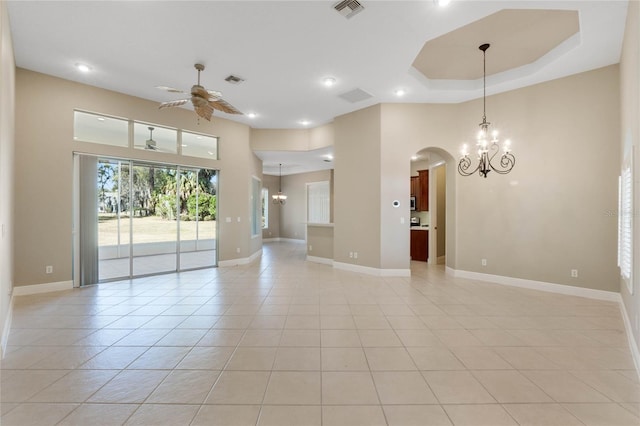 empty room featuring light tile patterned floors, a tray ceiling, and ceiling fan with notable chandelier